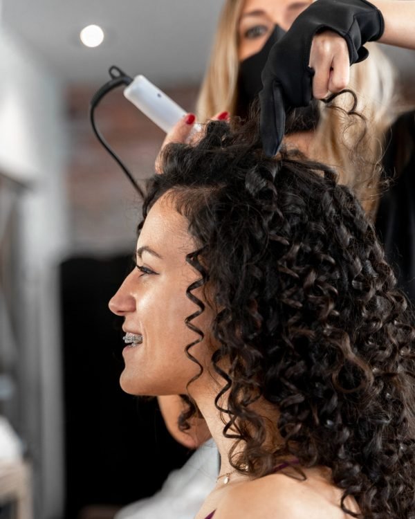 Close up and vertical photo of a hairdresser curling the hair of a woman in a salon